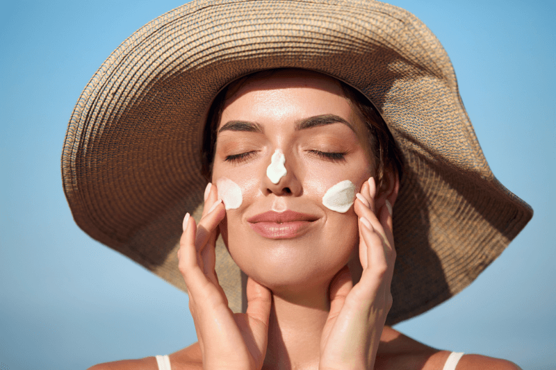 Persona che applica la crema solare sul viso sotto il sole estivo.