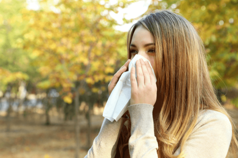 Donna all’aperto che si soffia il naso con un fazzoletto a causa delle allergie di fine estate.