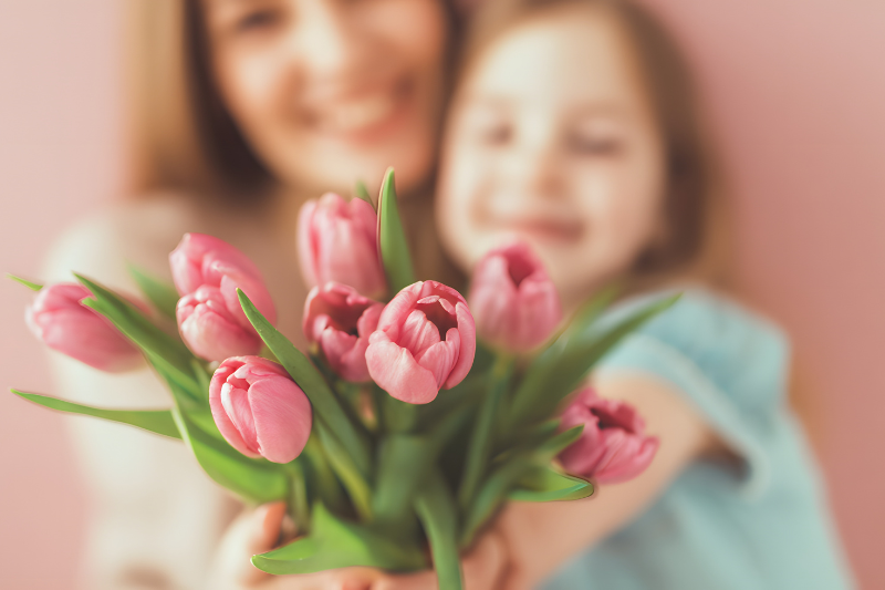 Bambina che regala un mazzo di tulipani rosa alla mamma, simbolo di affetto e Festa della Mamma