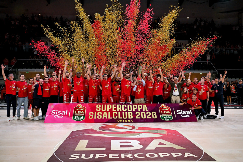 La squadra dell'Olimpia Milano festeggia sul parquet la vittoria della Supercoppa Italiana 2026, tra coriandoli rossi e dorati e con il trofeo al centro della celebrazione.