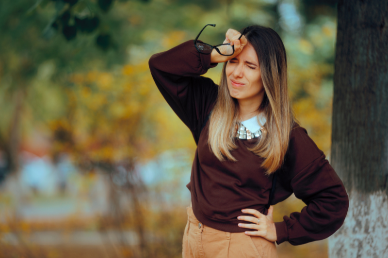 Donna all'aperto in autunno che si porta una mano alla fronte e appare affaticata, a rappresentare stanchezza e spossatezza legate al cambio di stagione